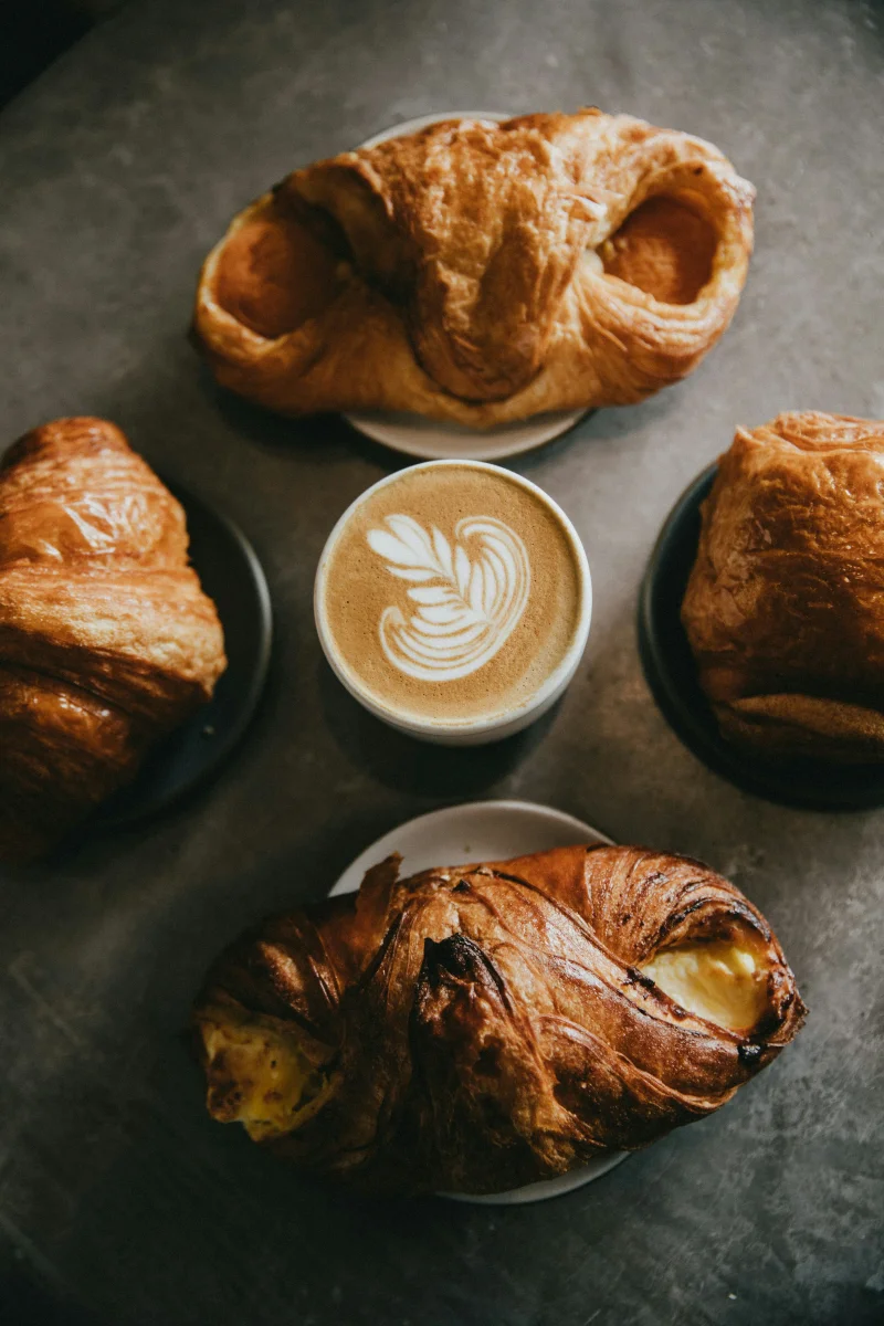 A cup with latte art surrounded by golden pastries.
