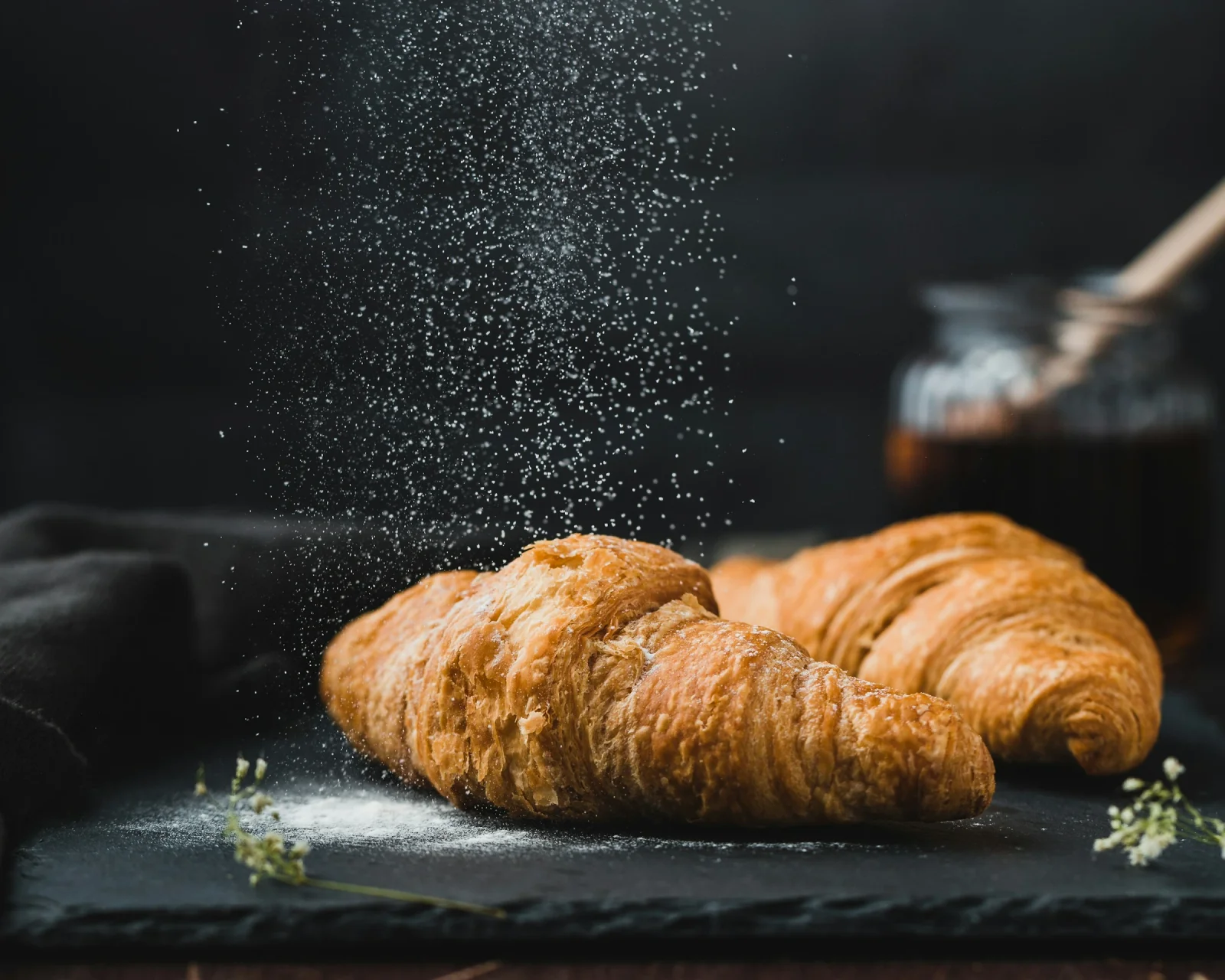 Two golden croissants on a dark tray, dusted with flour.